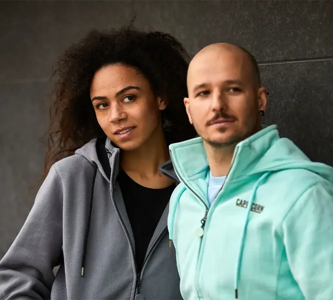 Weibliches Model mit grauer Kapuzenjacke und männliches Model mit mintfarbener Kapuzenjacke