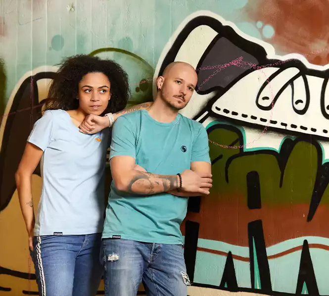 Frau mit hellblauem Shirt und Mann mit grünem Shirt vor Graffiti Wand stehend