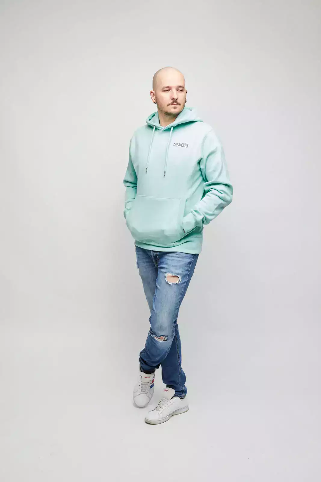 Männliches Model trägt mintfarbenen Hoodie mit Logo in grau auf Brust. Vorderansicht.