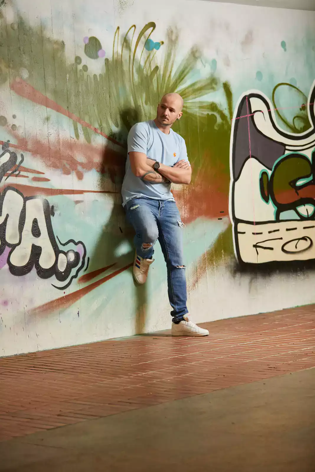 Model stehend mit hellblauem T-Shirt vor Graffiti Wand