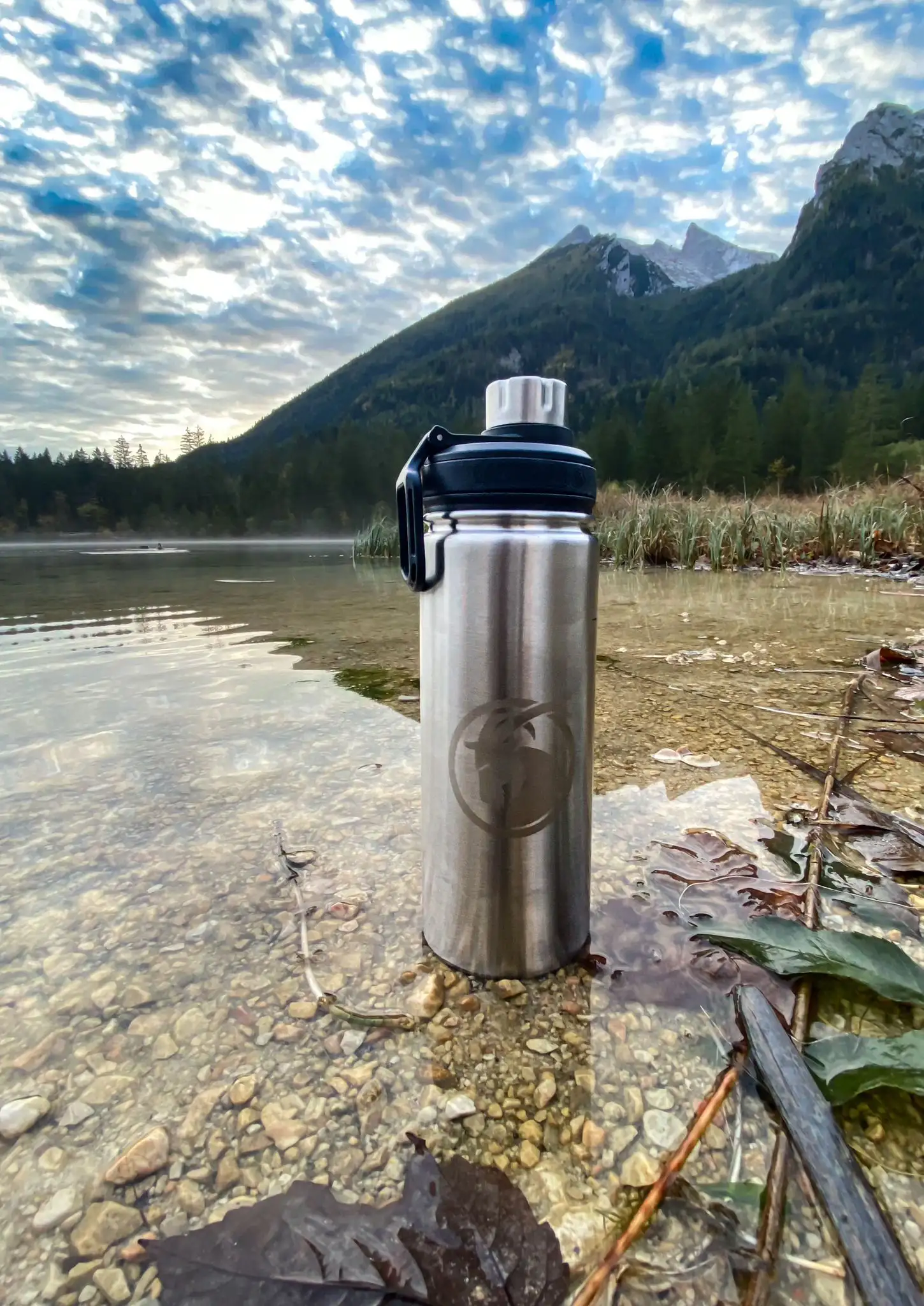 Edelstahl Trinkflasche am Flußufer mit Berg im Hintergrund