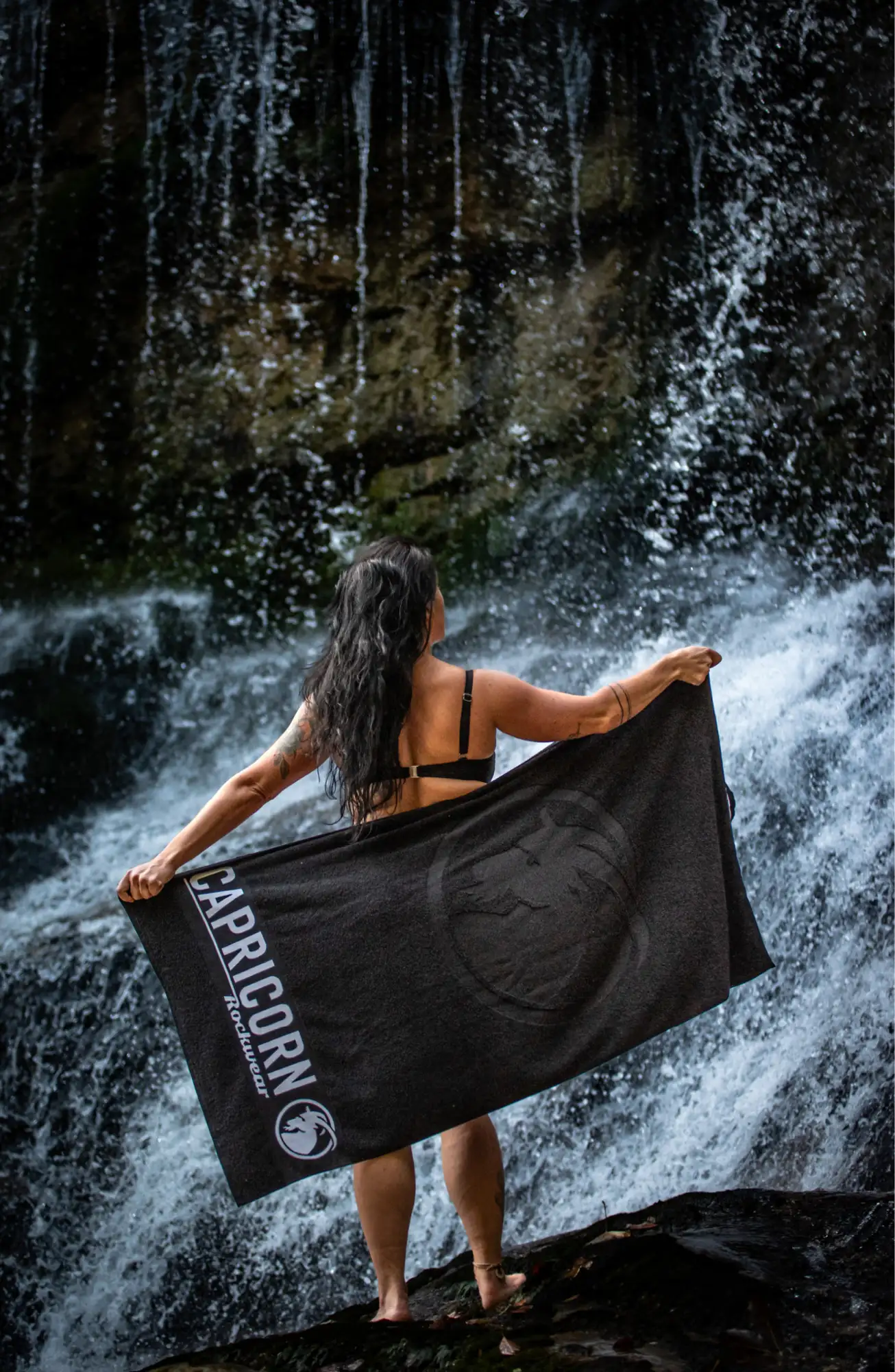 Frau vor Wasserfall mit schwarzen Capricorn Rockwear Handtuch
