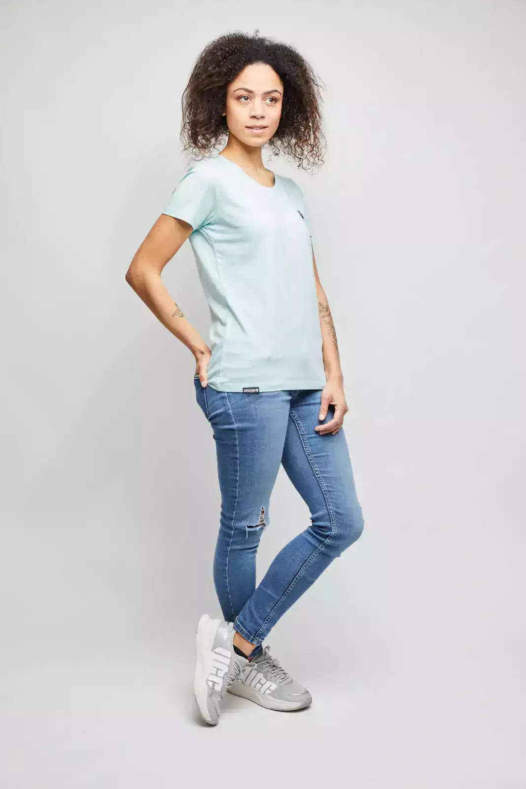 Frau trägt mintfarbenes Frauen T-Shirt vor weißer Wand. Studioaufnahme