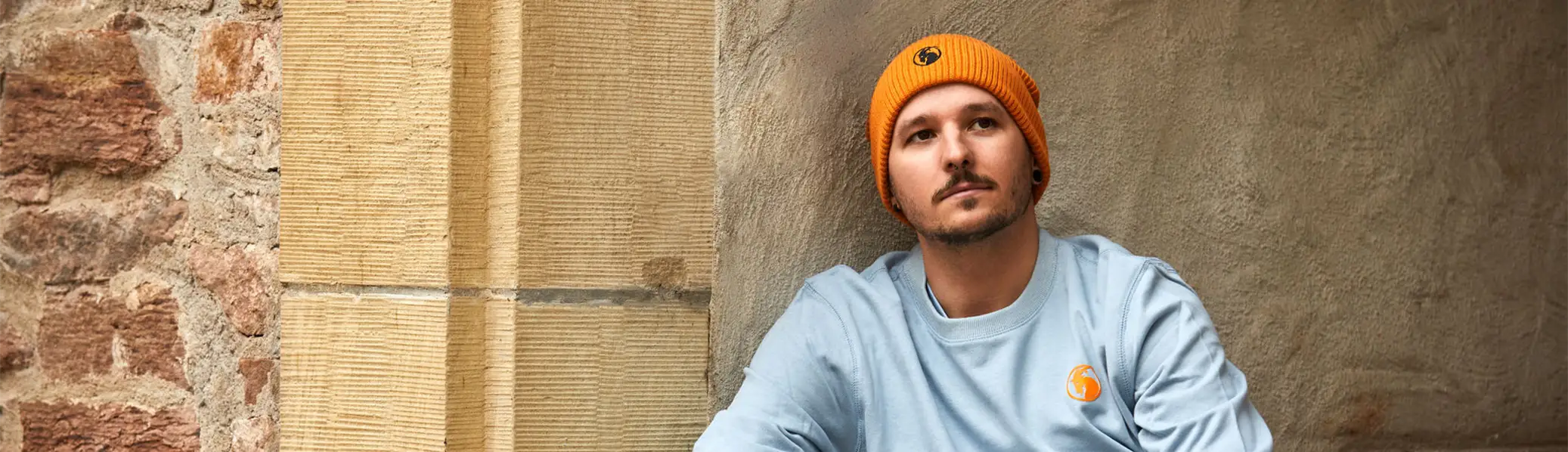 Beanie orangefarben präsentiert von männlichem Model auf Treppe sitzend