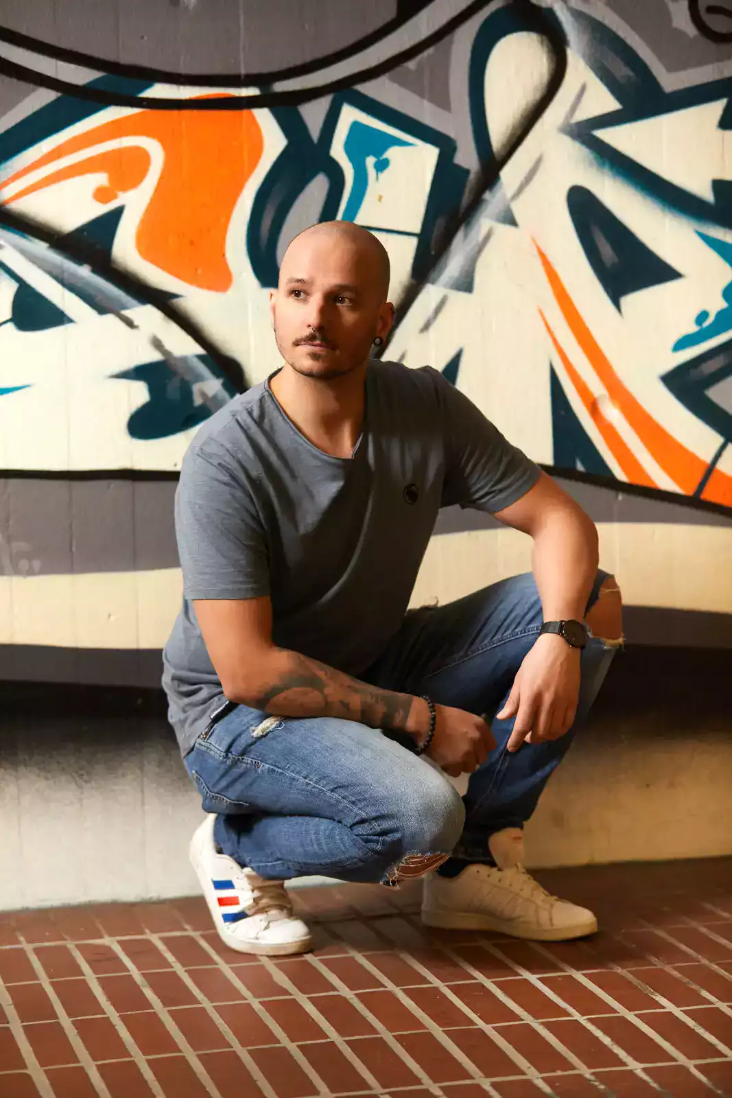 Mann mit grauem T-Shirt vor Graffiti Wand kniend