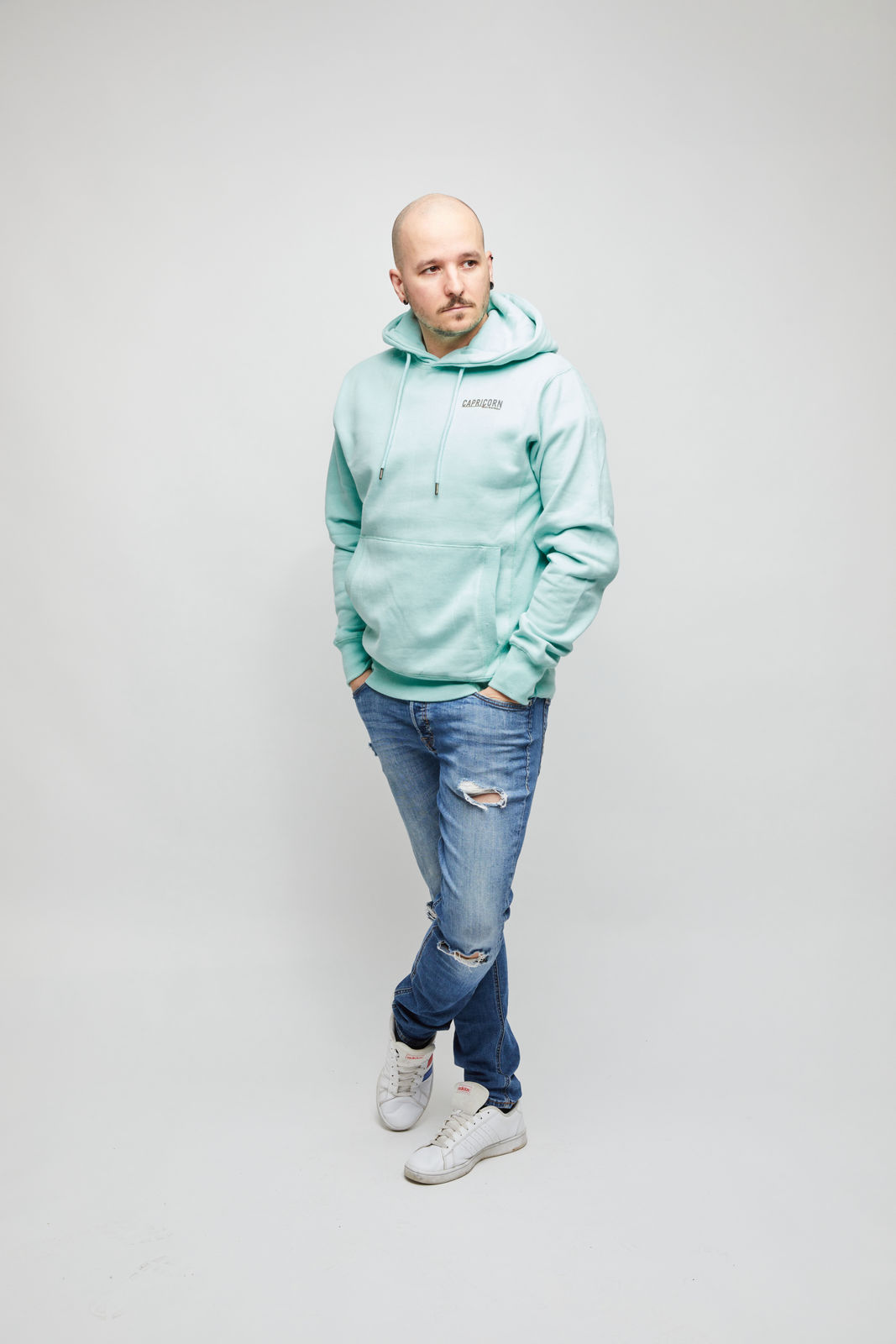 Männliches Model mit mintfarbenem Hoodie. Dunkelgraues Logo auf der Brust. Vorderansicht.