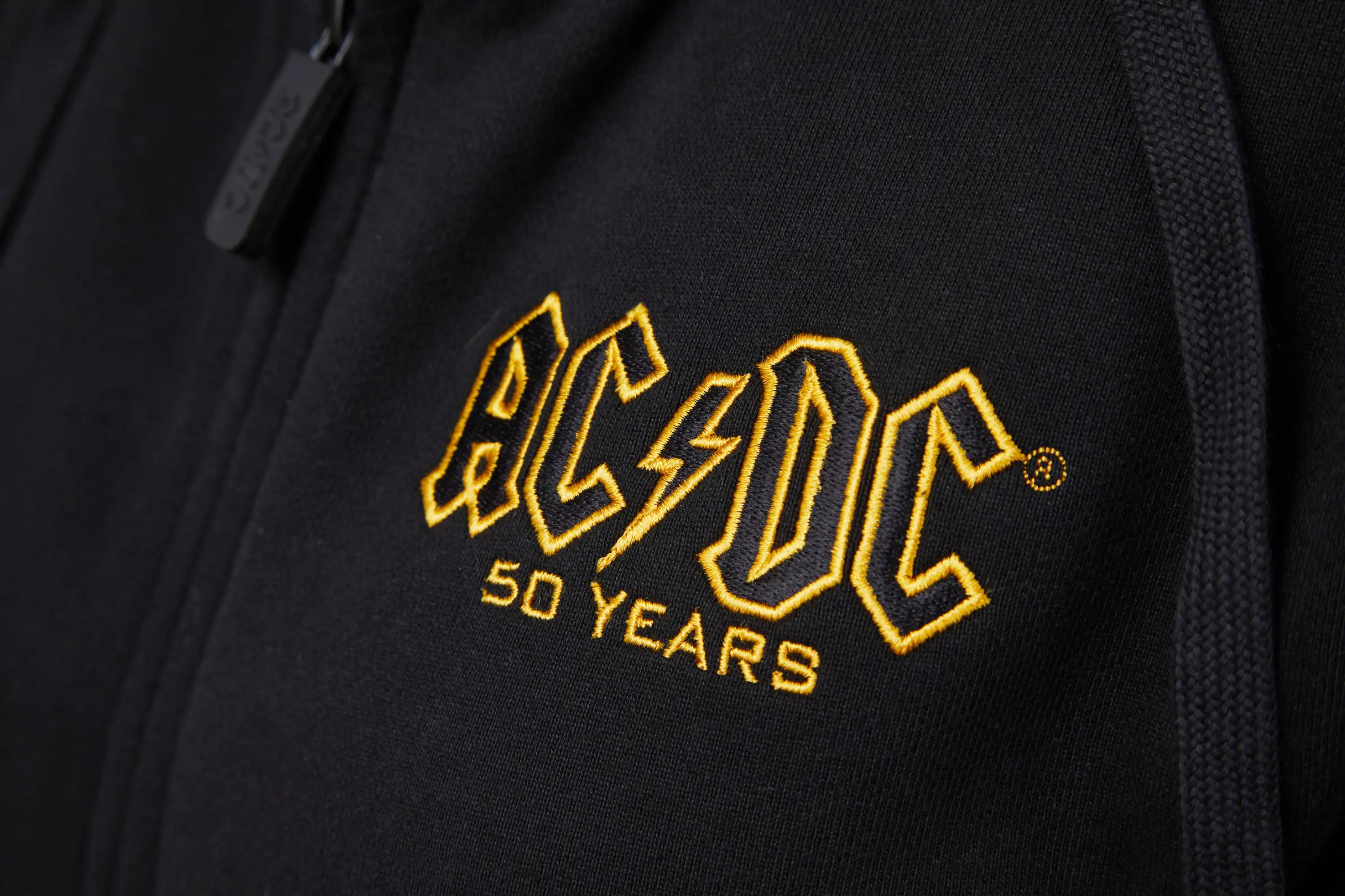 Detailansicht AC/DC Logo in schwarz gold Bruststick