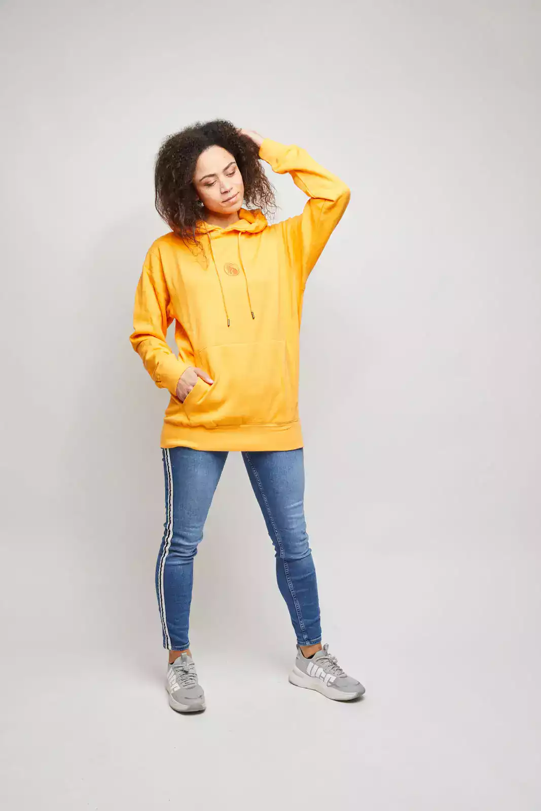 Frau trägt orangefarbenen Hoodie und streicht sich mit der Hand durch die Haare. Studioaufnahme