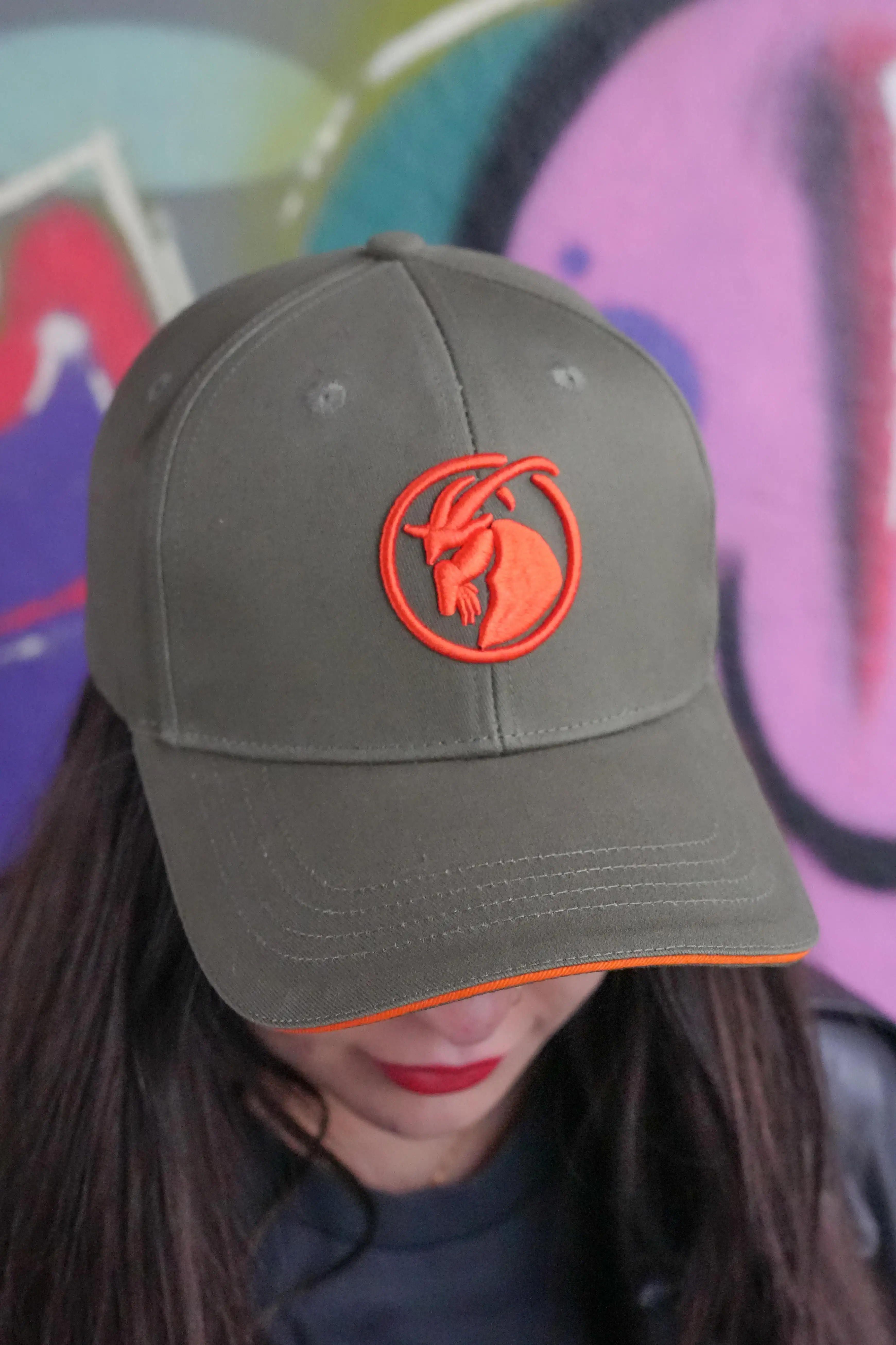 olivfarbene Baseballcap mit orangefarbenem Steinbock Stick. Ansicht von oben