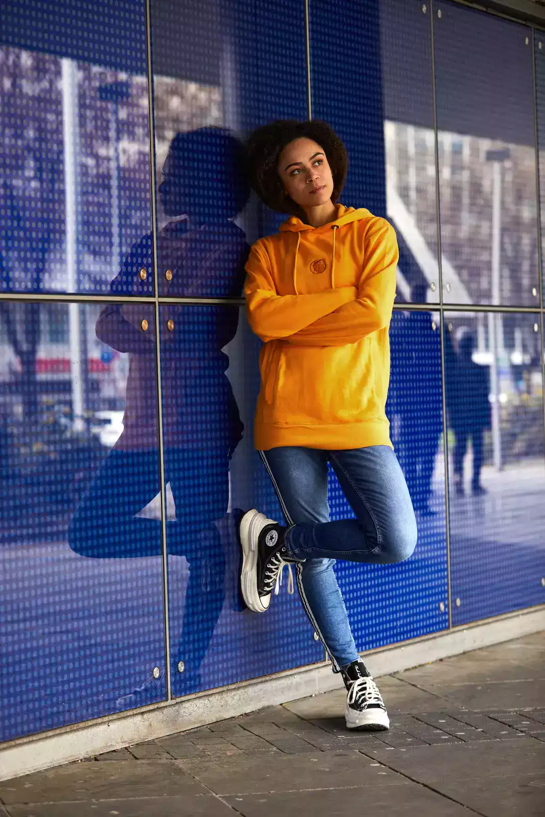 Frau trägt orangefarbenen Hoodie vor einer blauen Wand