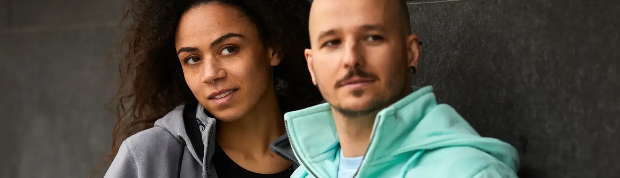 Frau mit grauer Kapuzenjacke und Mann mit mintfarbener Kapuzenjacke. Nahaufnahme