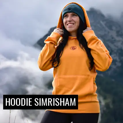 Frau trägt orangen Hoodie Simrisham in einer Berglandschaft 