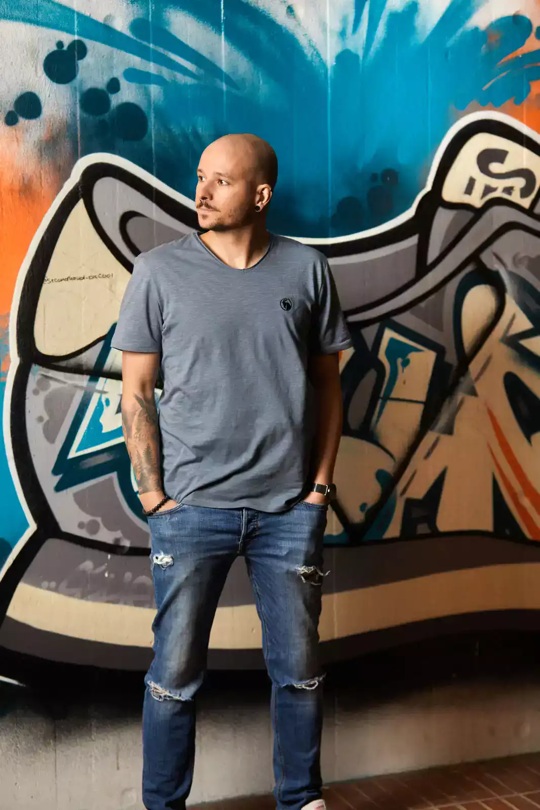 Mann trägt graues Shirt vor Graffiti Wand stehend