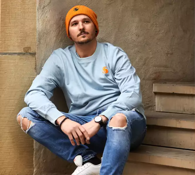 männliches Model in hellblauem Sweatshirt und orangefarbener Beanie