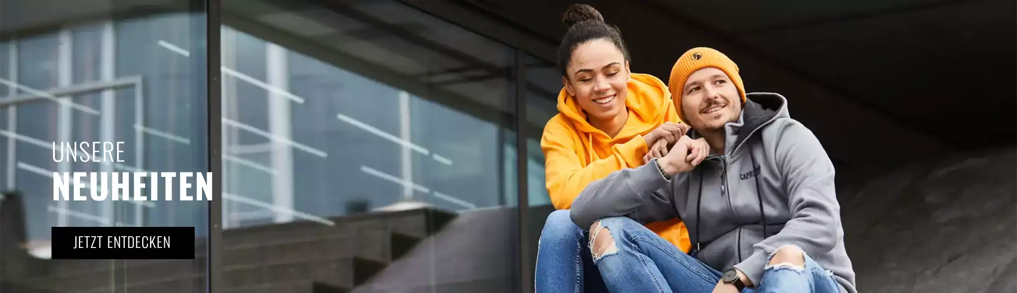 Frau in orangenem Hoodie neben einem Mann in grauem SweatshirtNeuheiten bei Capricorn Rockwear