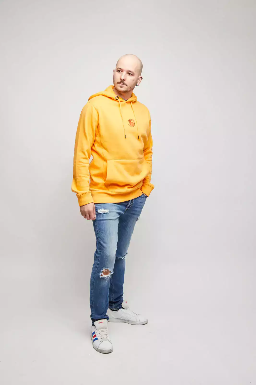 Männliches Model trägt orangefarbenen Hoodie mit zentralem Logo Stick. Vorderansicht.
