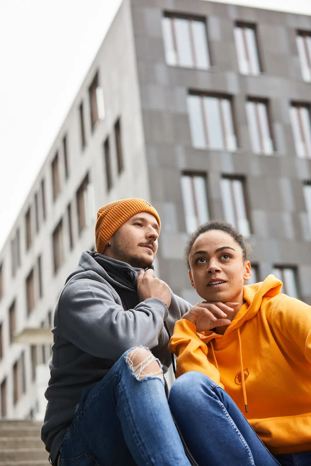 Mann mit grauem Hoodie und Frau mit orangefarbenen Hoodie auf Treppe sitzend