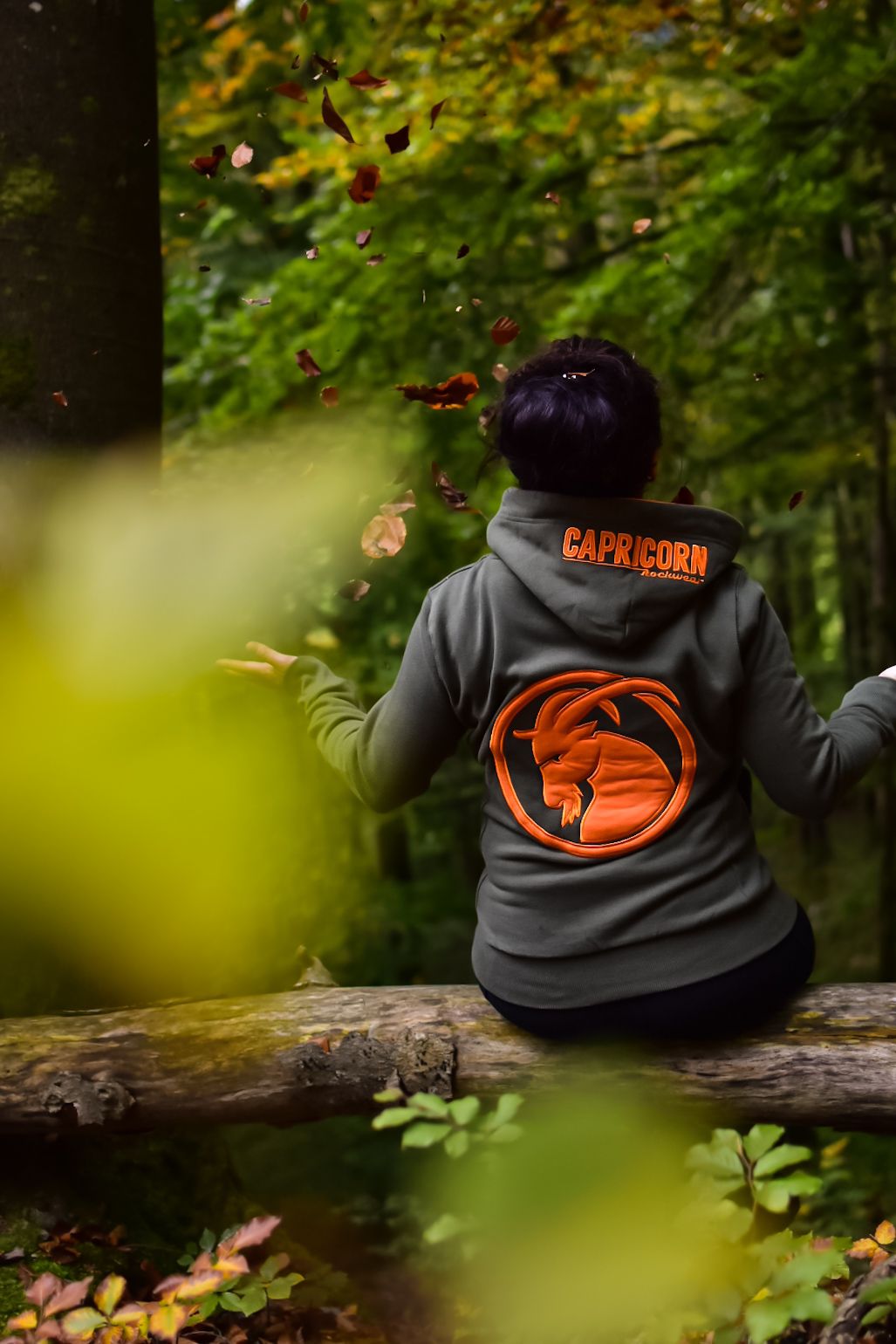 Hoodie olivgrün mit orangefarbenem Steinbock Kopf von Frau getragen, Bild im Wald