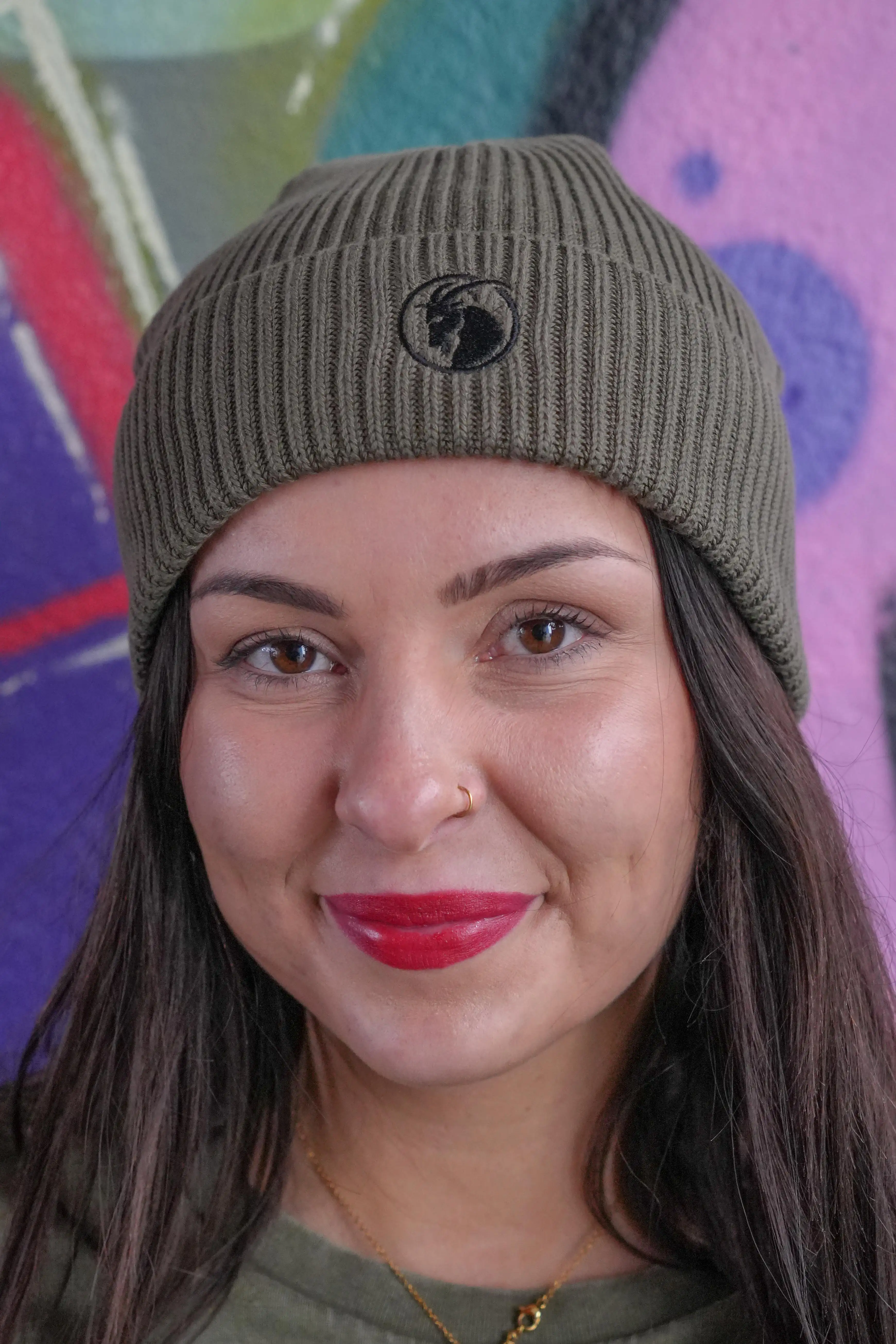 Beanie olivgrün mit schwarzem Steinbock Stick getragen von weiblichem Model