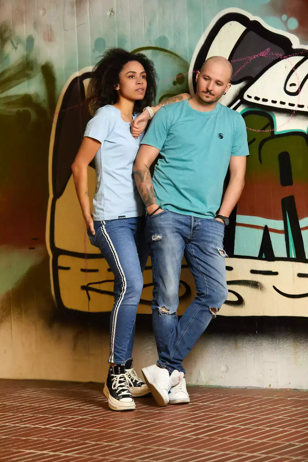 Frau mit hellblauem T-Shirt und mann mit grünem T-Shirt vor Graffiti Wand